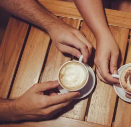 Close-up of two hands holding coffee cups with latte art on a wooden table, indoors.