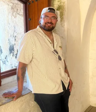 A happy caucasian man in a casual gray shirt smiling warmly at the camera indoors.