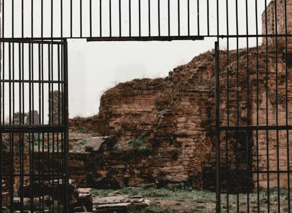 Captivating view of ancient stone ruins framed by a weathered iron gate, evoking history and nostalgia.