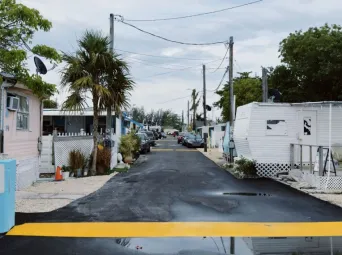 A quaint view of a mobile home park lined with palm trees and trailers under a cloudy sky.