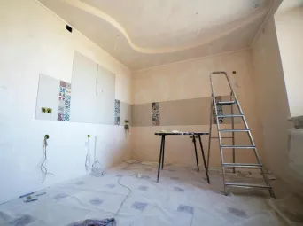 Interior view of a room under renovation with paint, tiles, and tools.