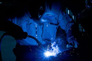 A welder using protective gear works with intense sparks flying.