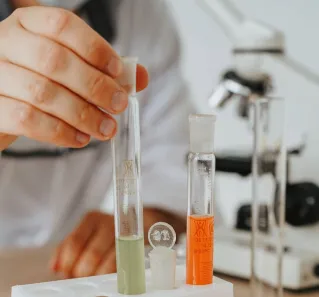 Close-up of scientist's hand arranging colorful test tubes with microscope in the background.