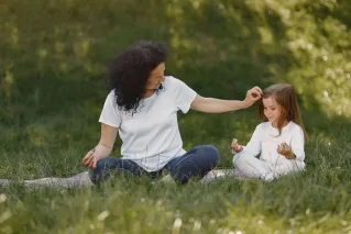 Mother and daughter bonding through yoga outdoors in a serene grassy field.