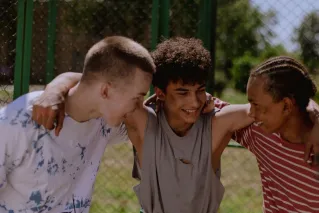 Happy teenagers laughing and embracing outside, showcasing friendship and diversity.