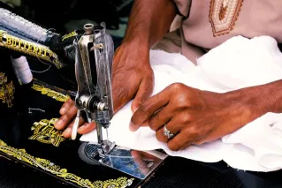 A skilled tailor sewing white fabric with precision on a vintage Butterfly sewing machine in Abuja, Nigeria.