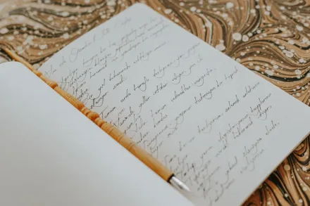 Open notebook with elegant handwriting placed on a marbled patterned surface, emphasizing creativity and artistry.