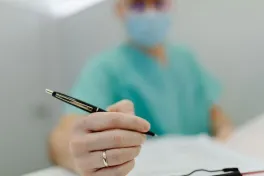 Close-up of a medical professional in scrubs writing with a pen, showing focus on hand and pen.