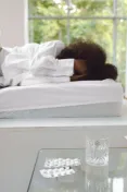 Woman lying in bed recovering, with medications on a glass table.