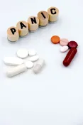 Assorted pills and tablets arranged next to wooden blocks spelling 'PANIC' on a white background.