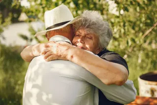 An elderly couple sharing a warm embrace in a sunny outdoor setting.