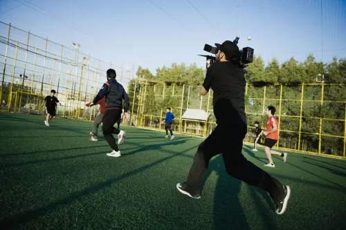 A dynamic scene of a camera crew capturing an intense soccer match on a sunny day.