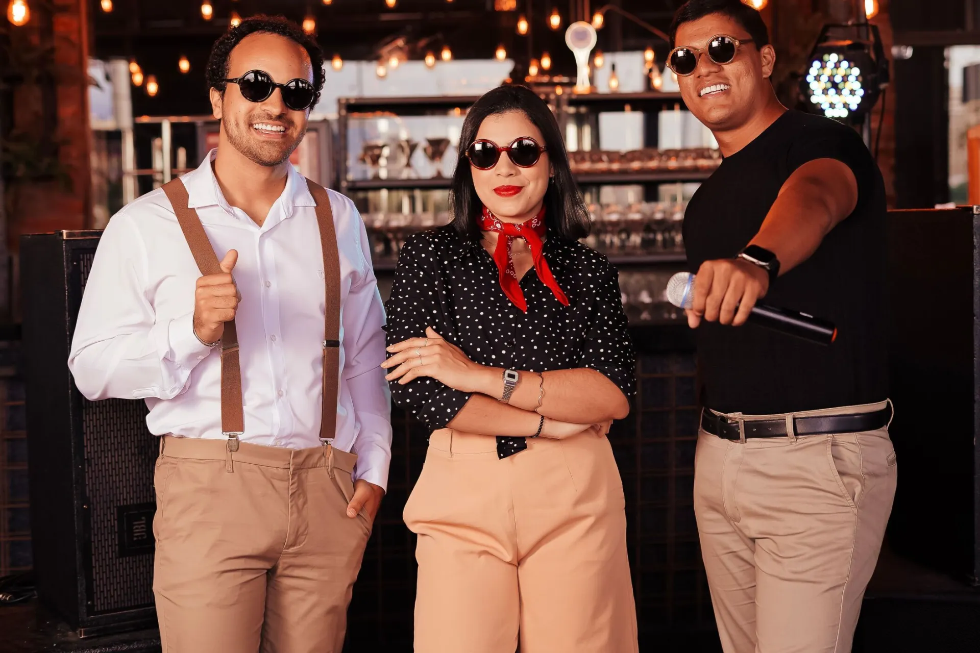 Three adults posing confidently indoors with stylish outfits and sunglasses.