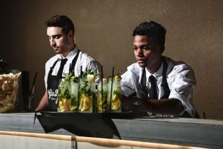 Two bartenders in formal attire preparing refreshing lemonades on a bar counter indoors.