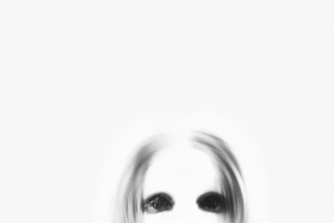 A ghostly figure with black eyes emerges from a blurred white background, creating a spooky atmosphere.