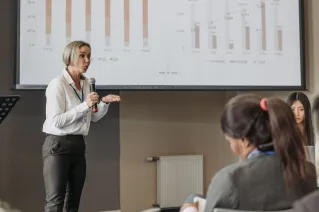 A professional woman leads a seminar on revenue analysis, engaging participants with graphs and data.