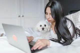 Woman uses laptop while relaxing with her pet dog in a cozy indoor setting, capturing the essence of remote work.
