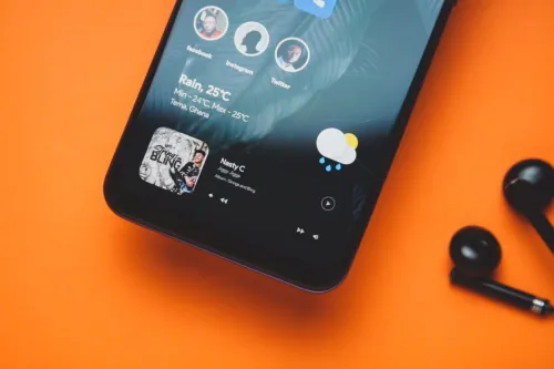 Close-up of a smartphone with earphones on an orange background showing a music playlist and weather update.