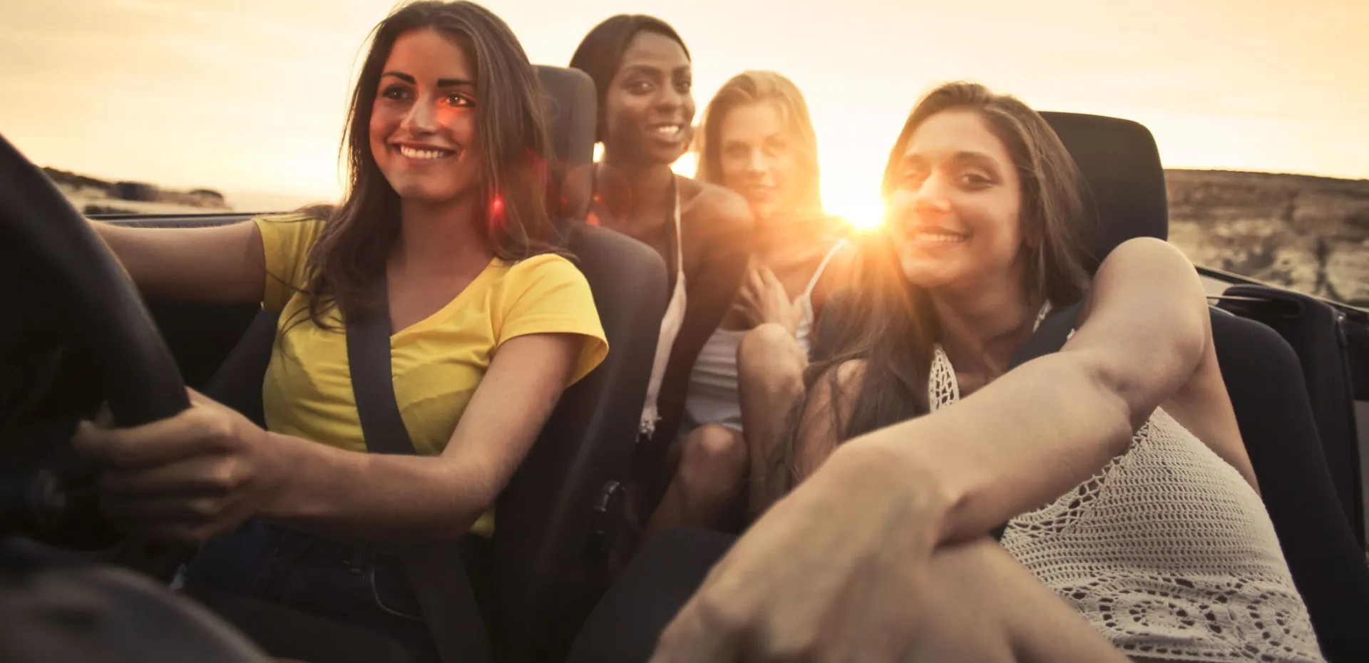 Four friends share smiles and laughter in a convertible during a sunset road trip in Malta.