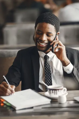 Smiling businessman talking on phone while taking notes in a modern office setting.