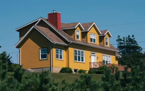 A vibrant yellow house nestled in the countryside of Percé, QC, Canada, surrounded by lush greenery.