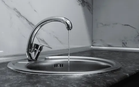 Chrome faucet with running water in a modern kitchen with marble countertop.