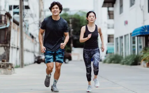 Energetic couple jogging outdoors in casual activewear in an urban environment, showcasing fitness and lifestyle.