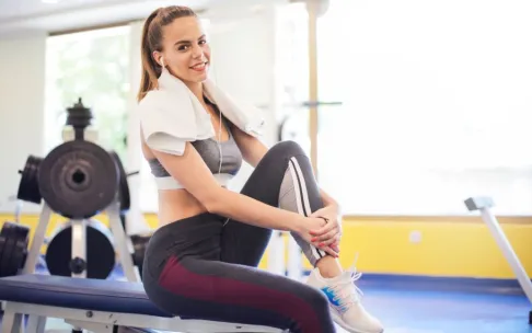 Active woman sitting with a towel around neck in a gym setting, embodying fitness and wellness.