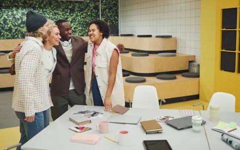A diverse group of colleagues huddling and smiling in a modern office setting, promoting teamwork.