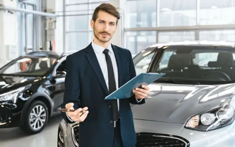 Professional car dealer in business suit holding clipboard in a bright car showroom.