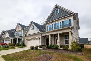 A row of modern suburban homes with garages, driveways, and landscaped lawns in daylight.