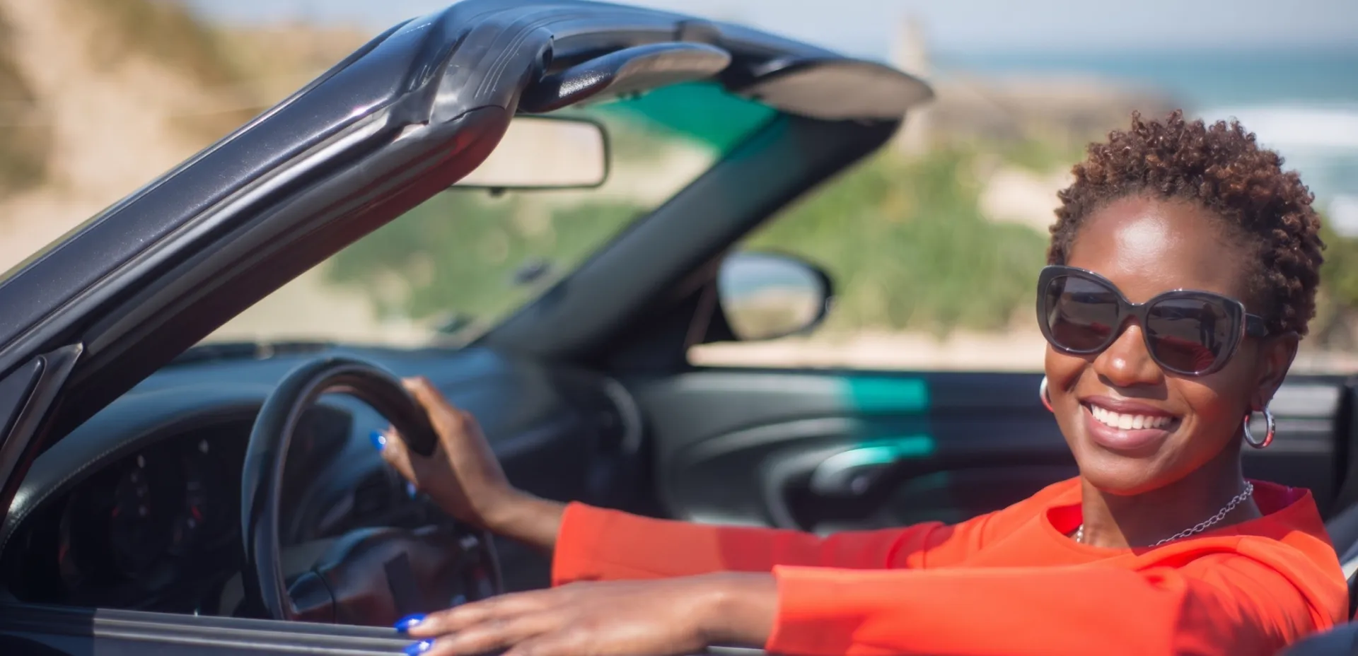 A cheerful woman enjoying a sunny drive in a convertible by the seaside.