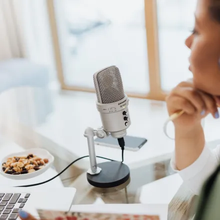 Woman using laptop and microphone for podcasting at home.