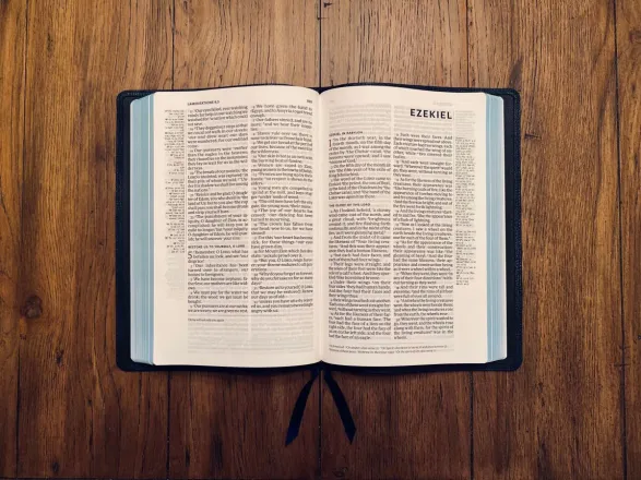 Open Bible displaying the Book of Ezekiel resting on a wooden surface.