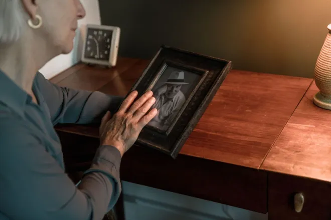 Senior woman nostalgically holding a framed photo, reflecting on memories.