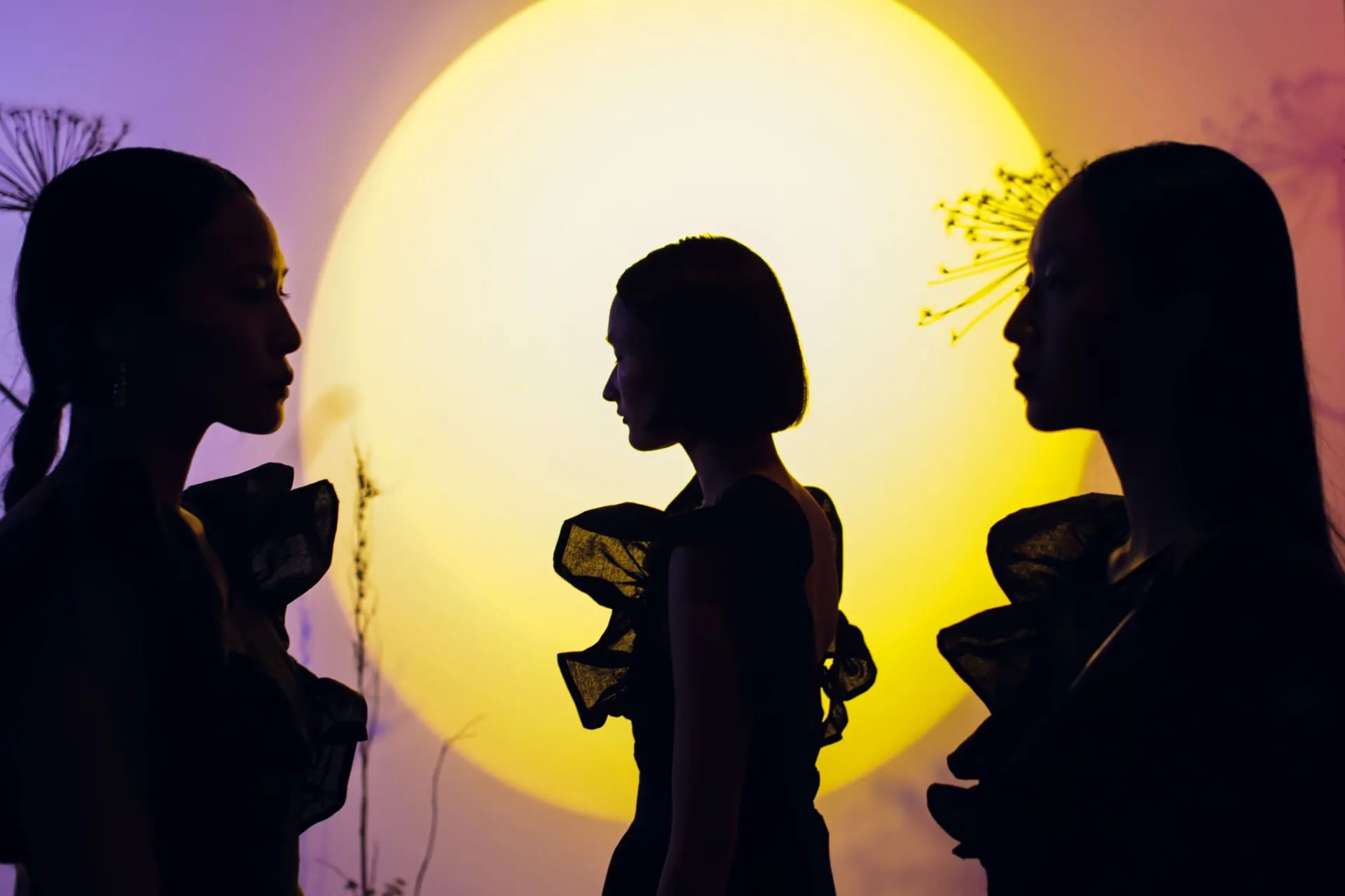 Three women in silhouette stand before a vibrant full moon backdrop, creating an artistic and conceptual scene.