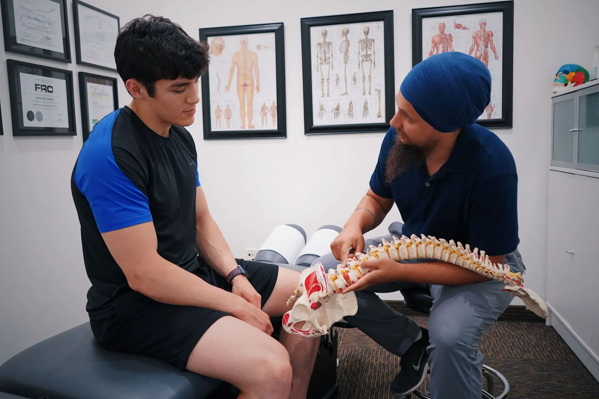 A doctor explains spinal issues to a patient using a spine model during a medical consultation.