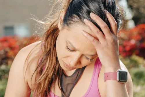 Close-up of a woman with a headache sitting outdoors wearing a smartwatch.