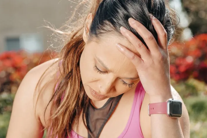 Close-up of a woman with a headache sitting outdoors wearing a smartwatch.