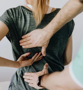 Top view of crop unrecognizable woman in casual wear showing chiropractor in eyeglasses and uniform pain spot on back while sitting on examination couch in hospital