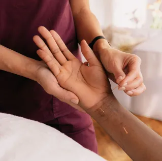 Close-up of hands performing acupuncture therapy on a patient in a spa setting.