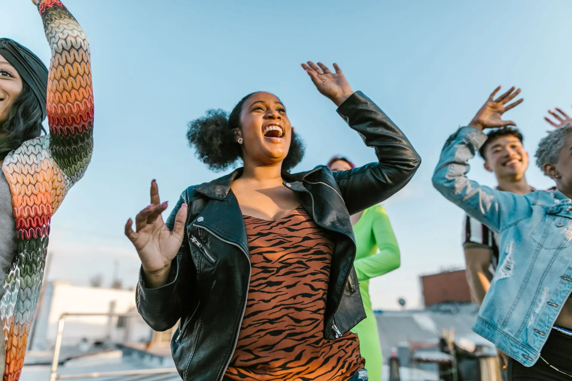 A diverse group of friends dancing and having fun on a rooftop during the day.