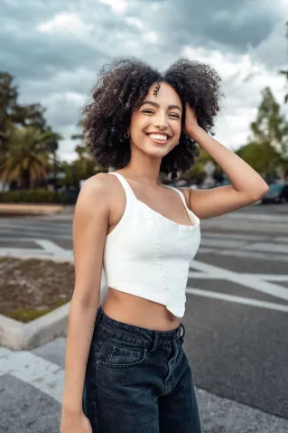 Portrait of a smiling woman with curly hair, standing outdoors in an urban area.