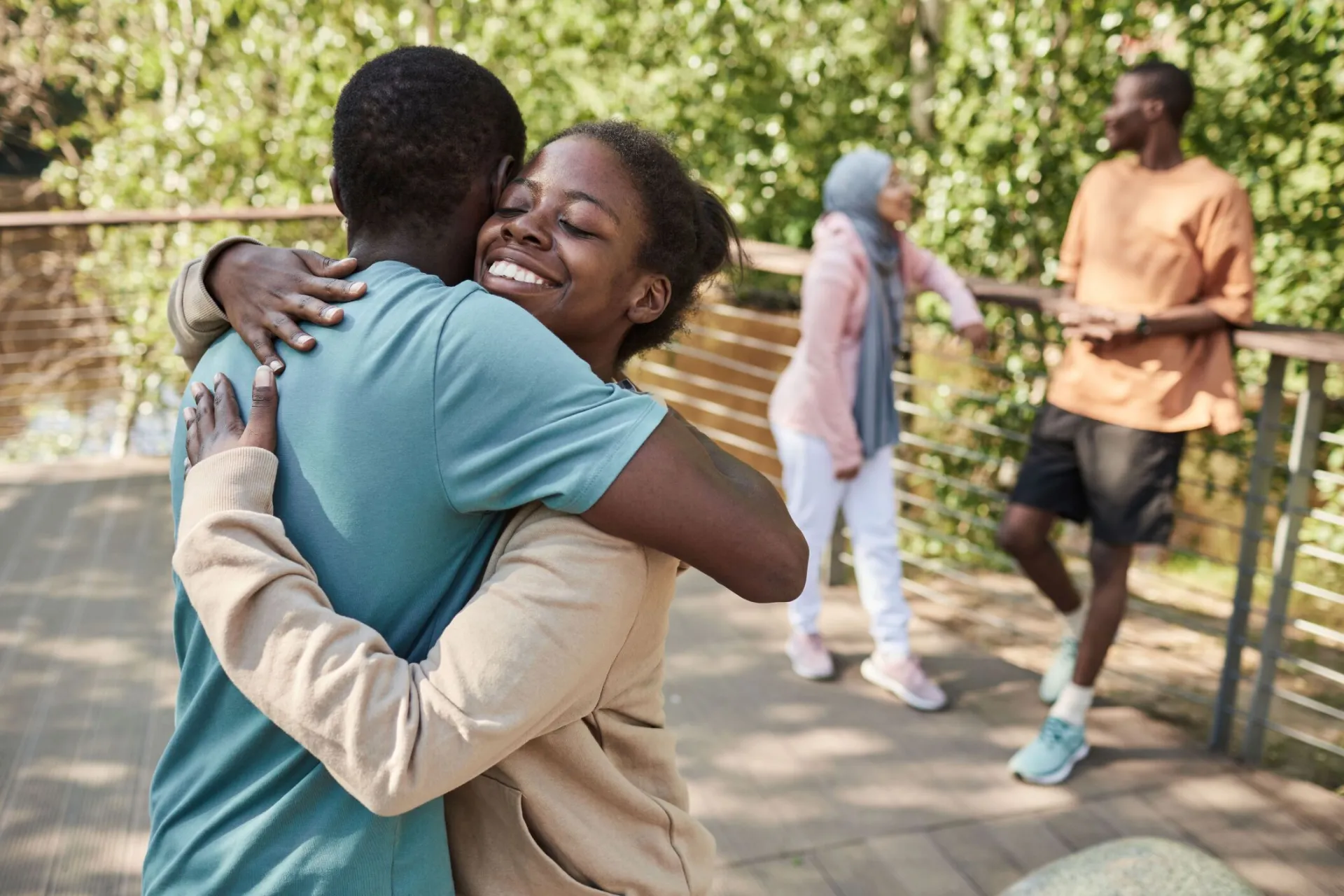 Joyful friends share a heartfelt embrace outdoors on a sunny day.