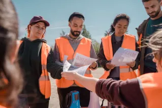 Group of volunteers in orange vests hold a community search meeting.