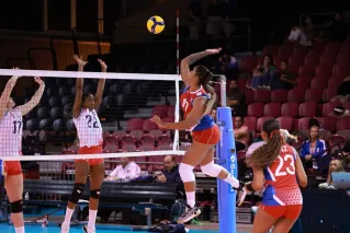 Dynamic action shot from a women's volleyball match with players in mid-air at the net.