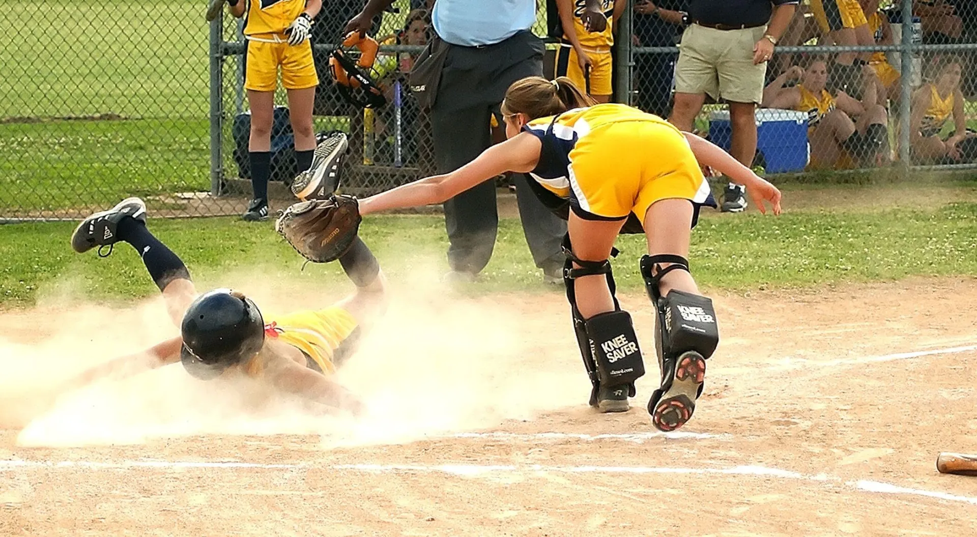 Youth softball player slides into home plate as the catcher attempts to tag. Sports action captured vividly.