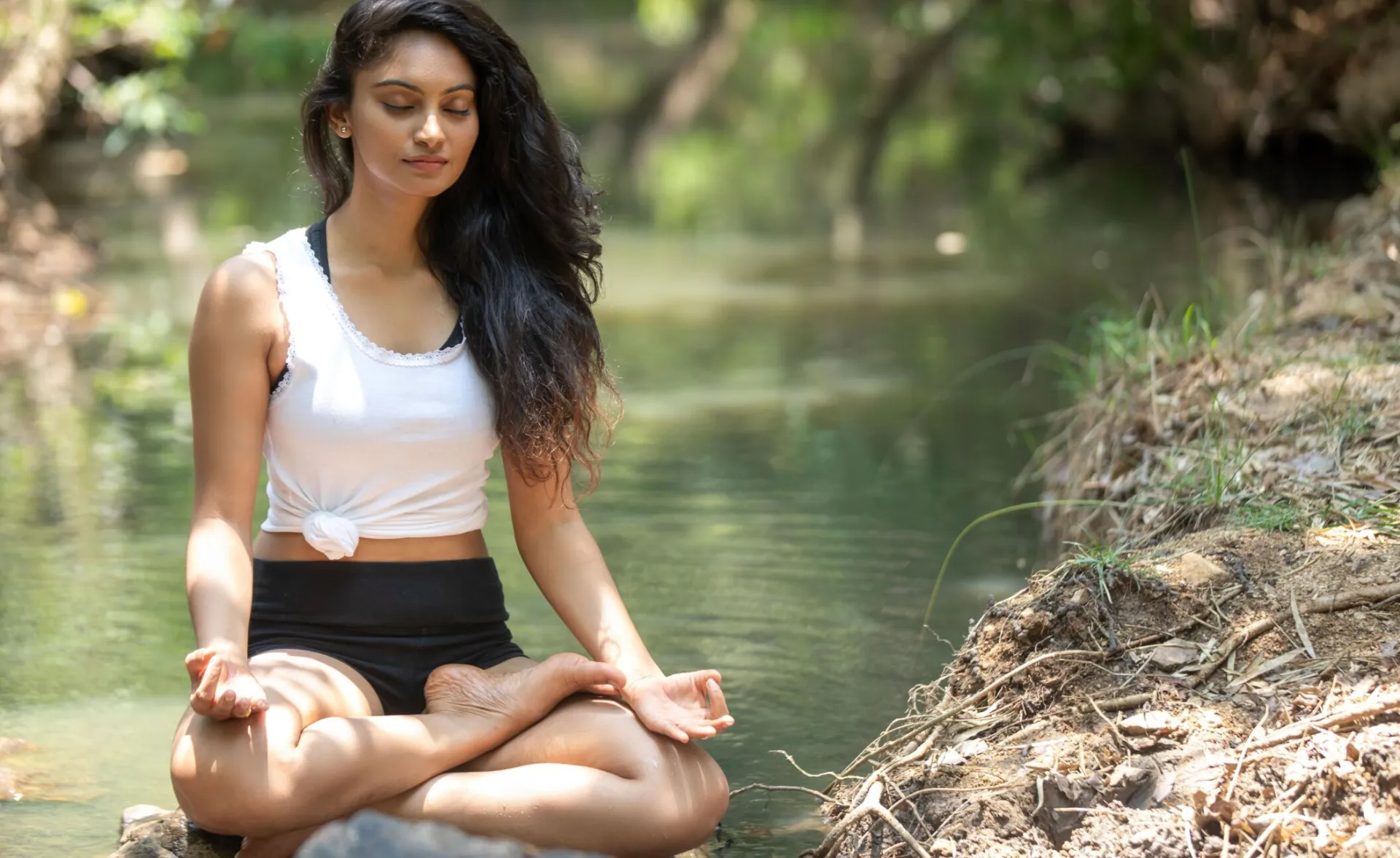 A serene scene of a woman meditating beside a peaceful river in nature.