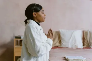 A serene image of a woman with closed eyes in prayer, capturing a moment of spiritual reflection indoors.