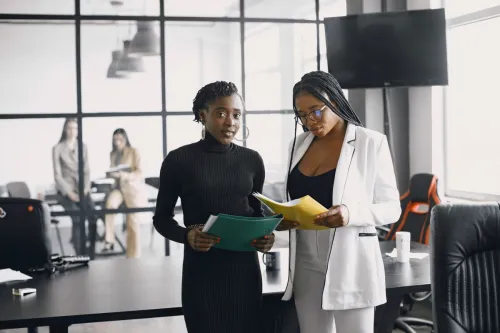Two professional women reviewing documents in a modern office setting.